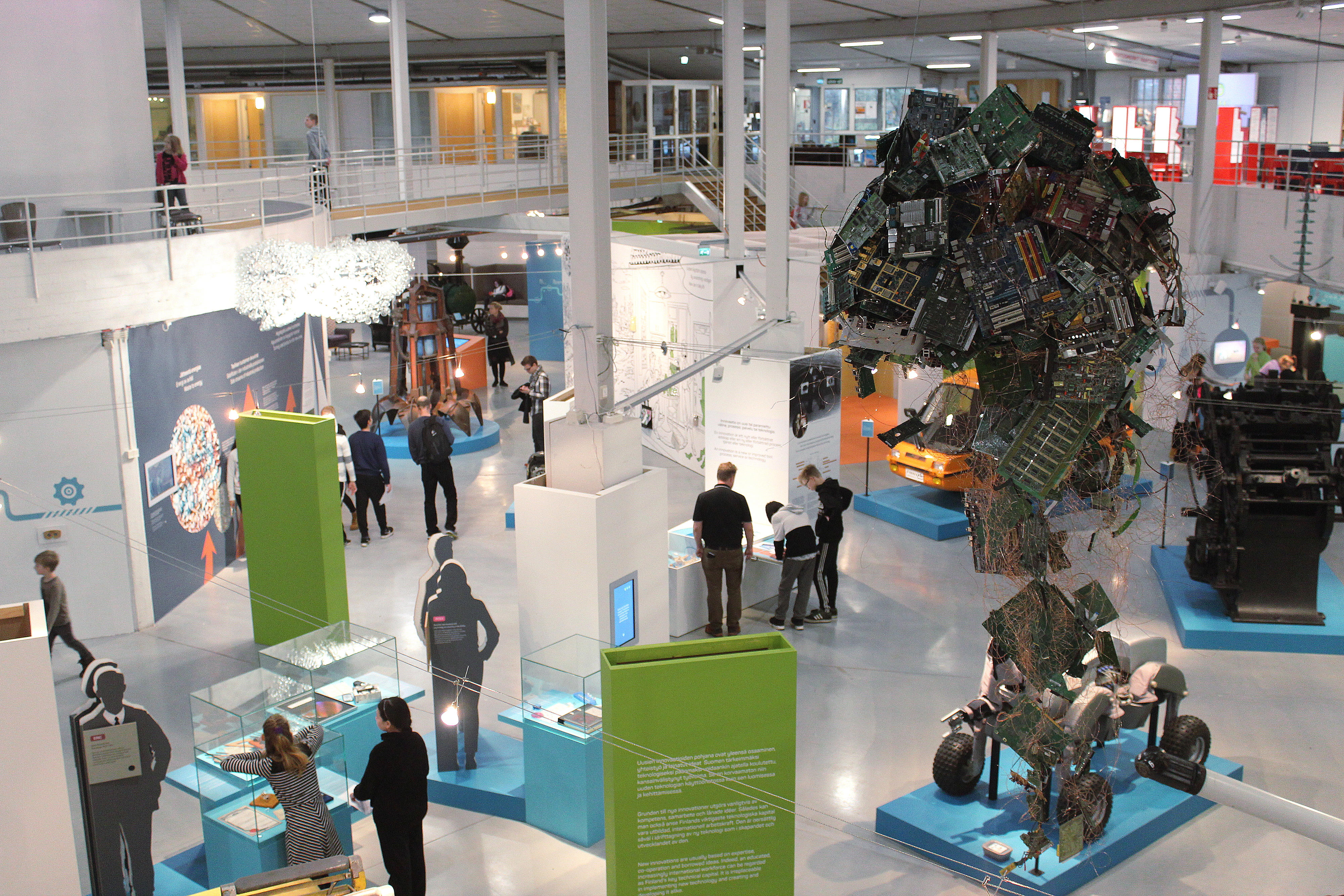 Tekniikan museon näyttelytiloissa vilisee ihmisiä, jotka seisoskelevat esineiden edessä kirkkaassa valaistuksessa.