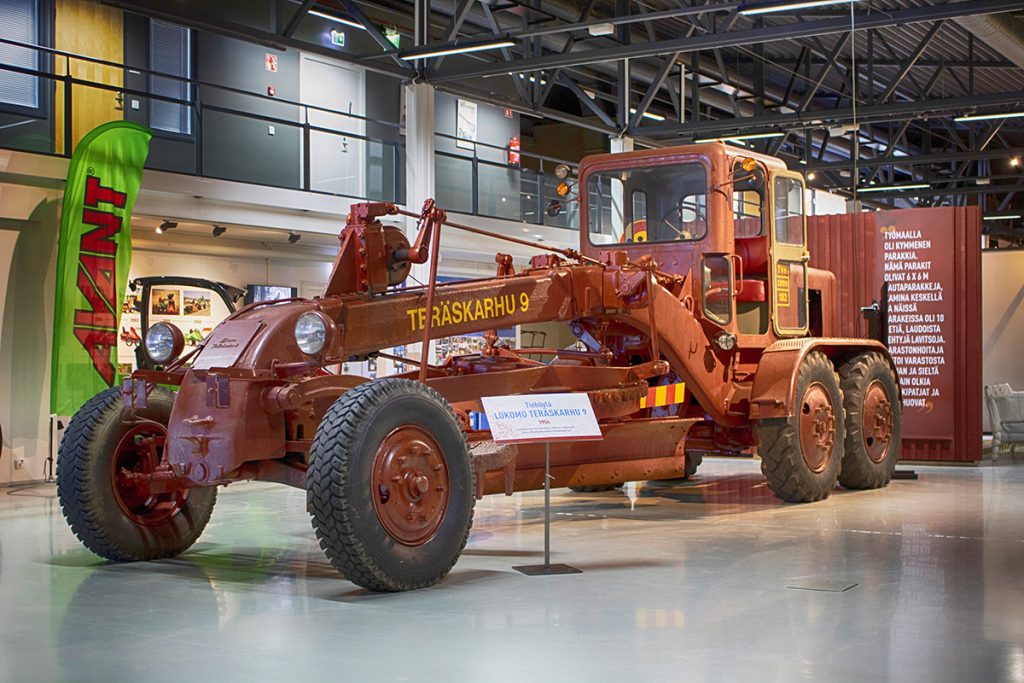 Tiilenpunainen Teräskarhu on massiiviinen tiehöylä, jossa on iso alusterän kehä ja kiinteä ohjaamo. Kuva on otettu Mobilian näyttelyssä.