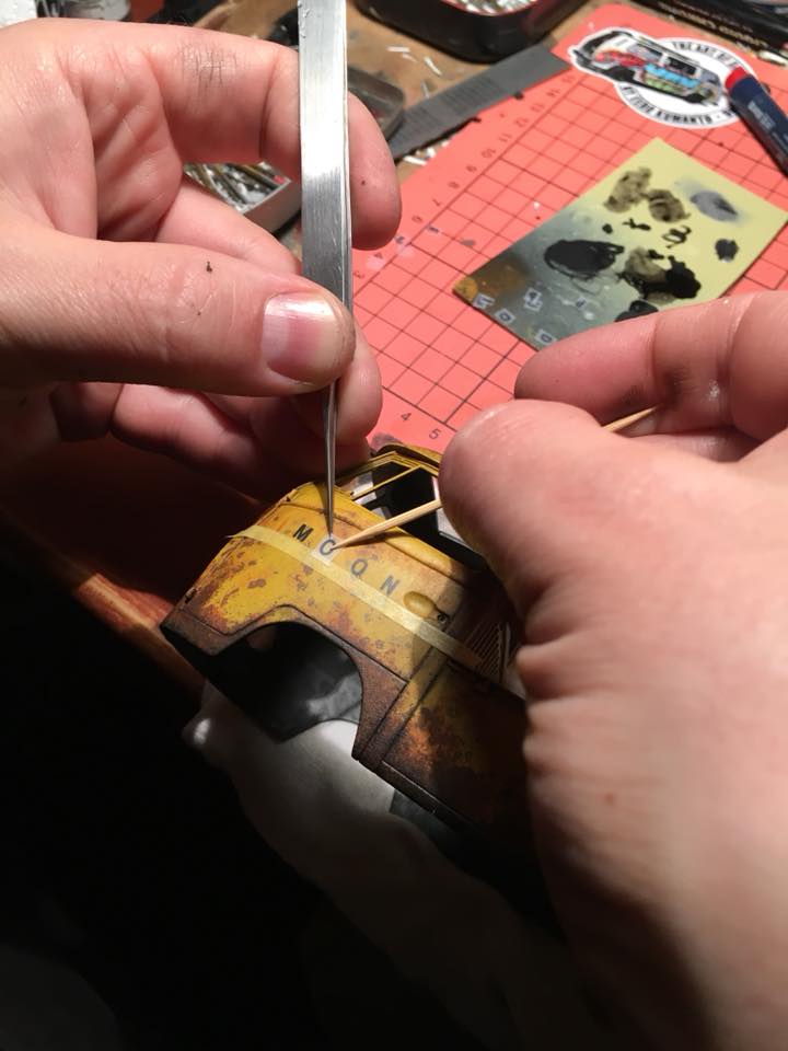 Pienoismallirakentajan kädet työssä, jossa tarraa kiinnitetään pinsetein ja hammastikulla. Työstettävänä Volkkarin pakettiauto.