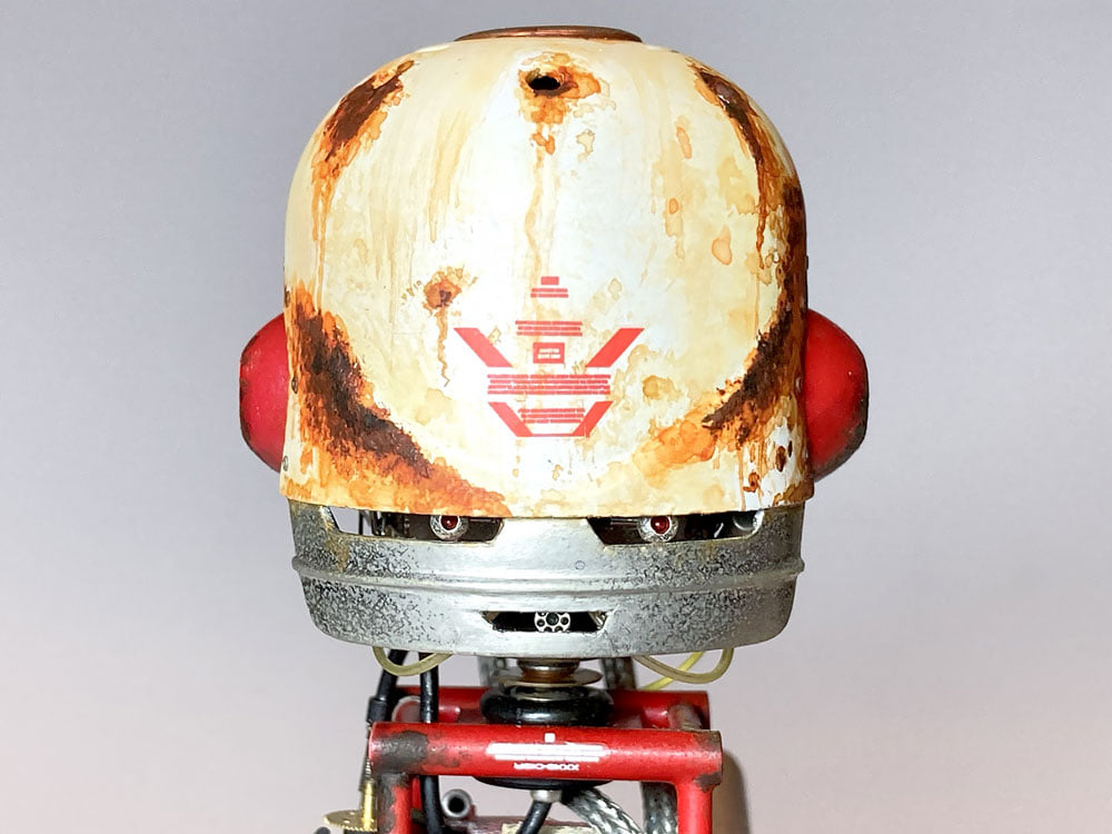 Robotin pää. Vaalea kypärä hopeanharmaiden robotin kasvojen päällä.