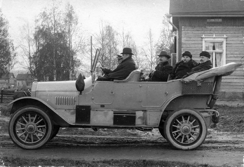 Mustavalkoisessa kuvassa 1910-luvun kanttiauto kuljettuna sivusta. Kuomu on laskettu alas ja takapenkillä useampi matkustaja.