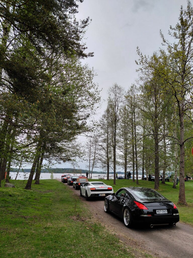 Rannalle johtavalla hiekkaväylällä pysäköintialueelle jonottaa useampi urheiluauto.